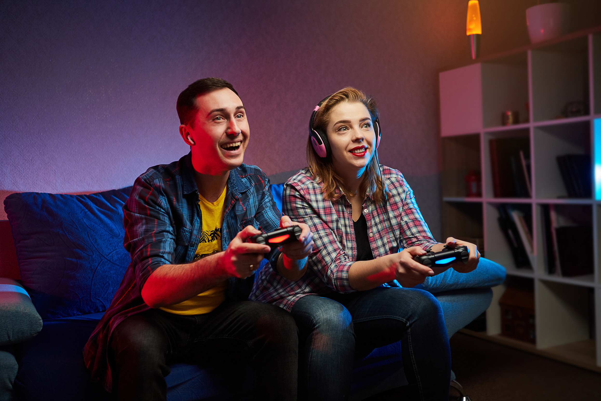 Portrait of crazy playful couple, Gamers enjoying Playing Video Games indoors sitting on the sofa, holding Console in hands Resting At Home, have a great Weekend